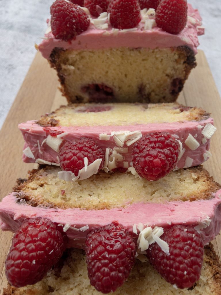 Sliced white chocolate and raspberries loaf cake on a wooden board